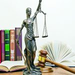 statue of justice on wooden table against the background of an open book.