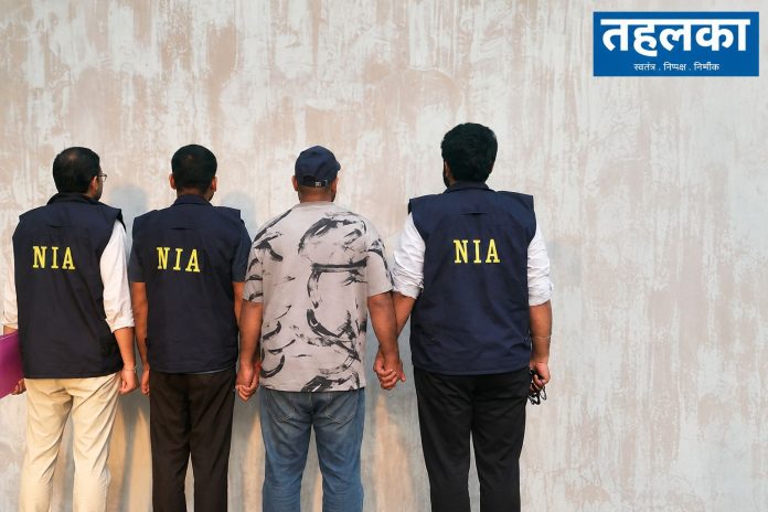NIA Officers Escort Detainee Against Wall विकास प्रभाकर हत्याकांड में एनआईए की जांच और यूएई से आरोपी की वापसी का प्रतीकात्मक दृश्य